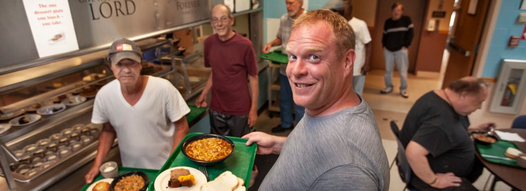 Jeffrey Blake poses while carrying a tray of food at Rescue Mission of Utica in New York